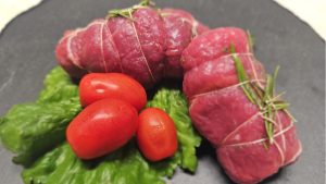 Pronti a cuocere di carne equina rolatine con rosmarino, legate con spago, serviti su foglia di lattuga con pomodorini freschi.